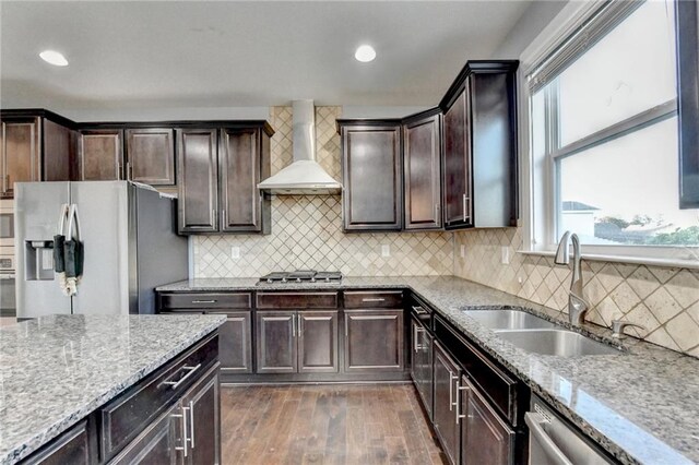 kitchen with sink, wall chimney exhaust hood, dark wood-type flooring, decorative backsplash, and appliances with stainless steel finishes