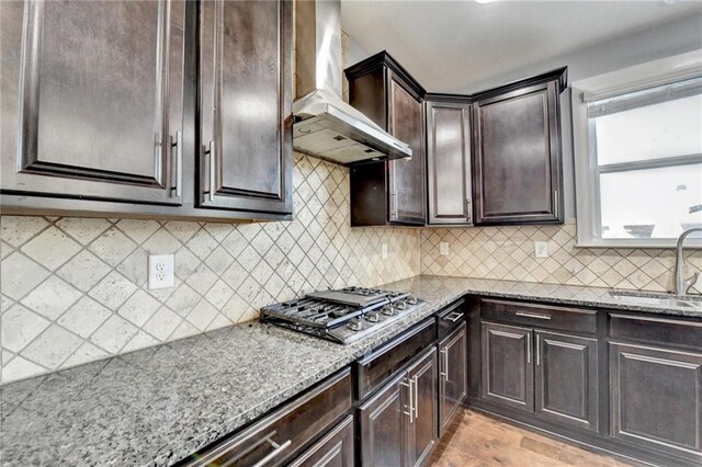 kitchen with sink, wall chimney exhaust hood, light wood-type flooring, light stone counters, and stainless steel gas cooktop