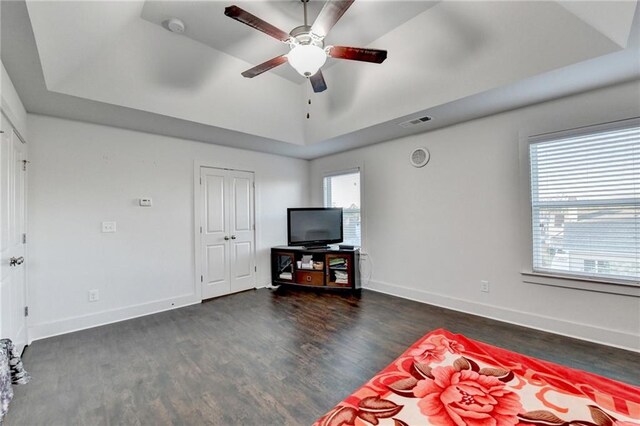 living room with a tray ceiling, ceiling fan, and dark wood-type flooring