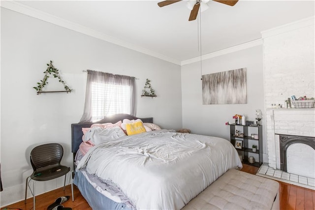 bedroom with ceiling fan, wood-type flooring, a stone fireplace, and ornamental molding