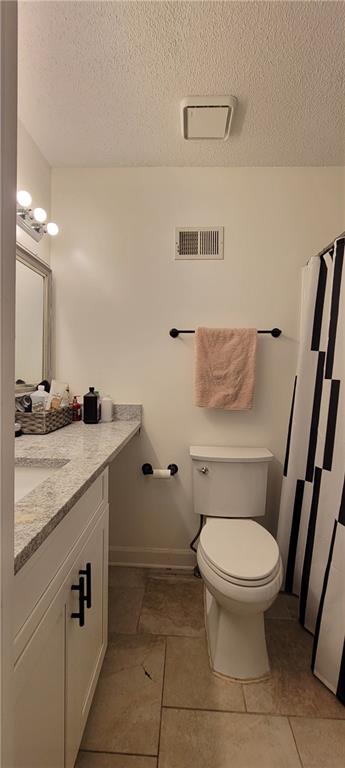 bathroom featuring tile flooring, a textured ceiling, toilet, and vanity