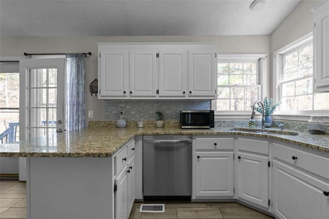 kitchen with appliances with stainless steel finishes, light stone counters, a peninsula, white cabinetry, and a sink