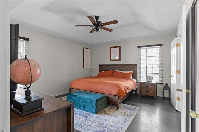 bedroom with a textured ceiling, baseboards, a raised ceiling, and wood finished floors