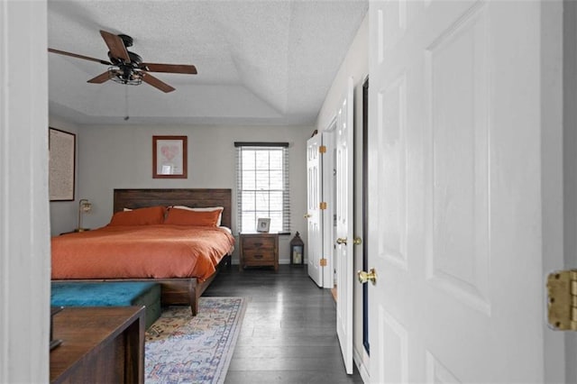 bedroom with dark wood-type flooring, a tray ceiling, ceiling fan, and a textured ceiling