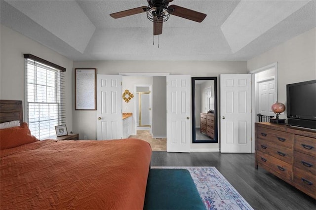 bedroom with a textured ceiling, ceiling fan, a tray ceiling, and dark wood-type flooring