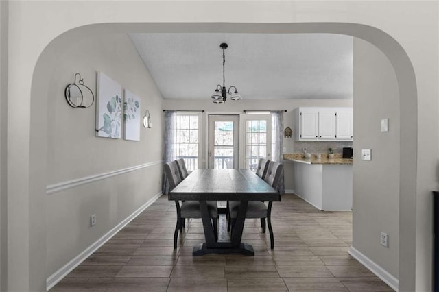 dining area featuring a chandelier, lofted ceiling, and baseboards