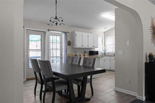 dining area with arched walkways, light wood-type flooring, a chandelier, and baseboards