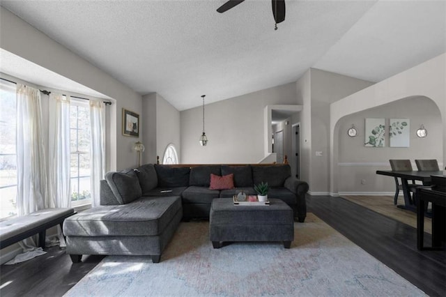 living area featuring lofted ceiling, arched walkways, a textured ceiling, wood finished floors, and baseboards