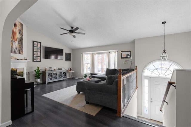 living area featuring baseboards, a ceiling fan, lofted ceiling, dark wood-style flooring, and a fireplace