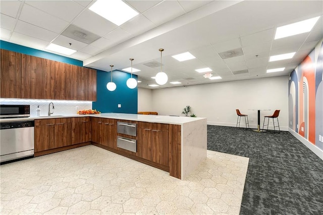 kitchen featuring kitchen peninsula, appliances with stainless steel finishes, a paneled ceiling, and pendant lighting