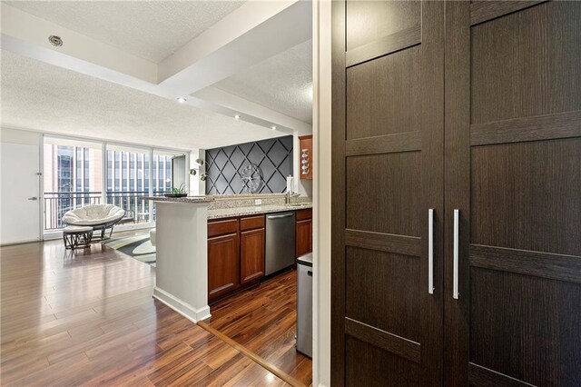 kitchen featuring stainless steel dishwasher, light stone counters, dark wood-type flooring, and a textured ceiling