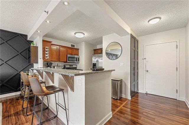 kitchen featuring a breakfast bar, dark hardwood / wood-style floors, light stone countertops, appliances with stainless steel finishes, and kitchen peninsula