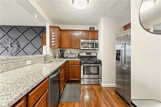 kitchen with light stone countertops, appliances with stainless steel finishes, a textured ceiling, sink, and hardwood / wood-style flooring