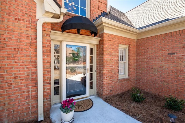 entrance to property with a shingled roof and brick siding