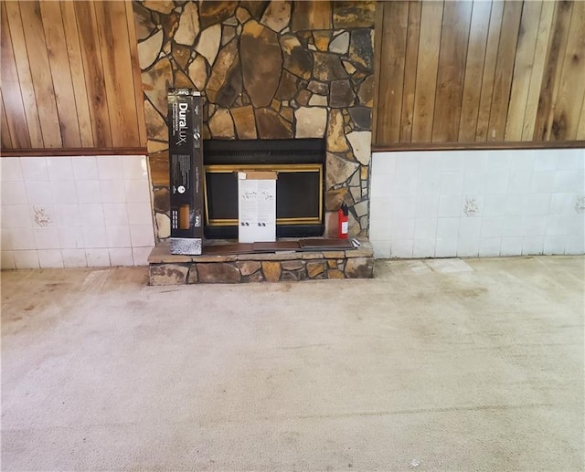 interior details with carpet floors, a stone fireplace, and wooden walls