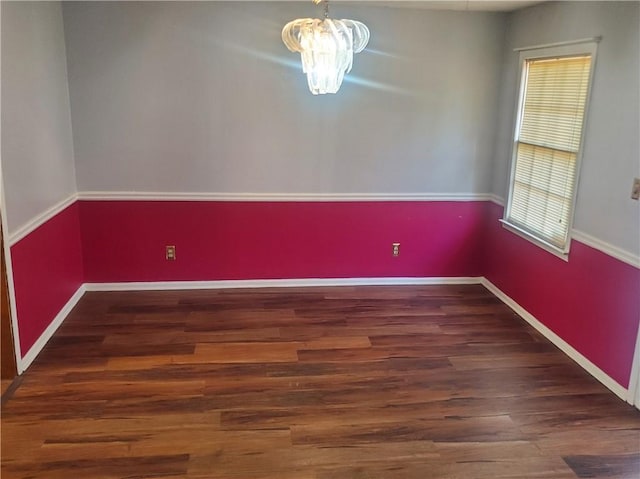 spare room featuring a chandelier and dark wood-type flooring