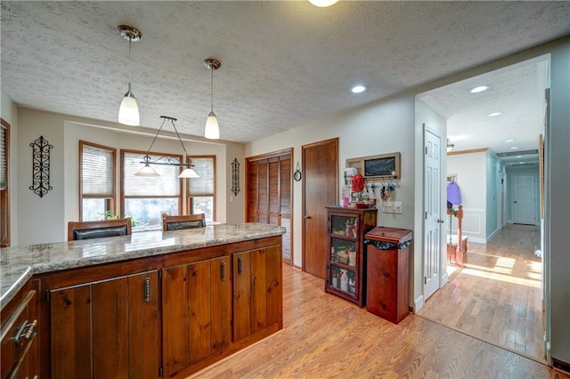 kitchen with light stone counters, hanging light fixtures, light hardwood / wood-style floors, and a textured ceiling