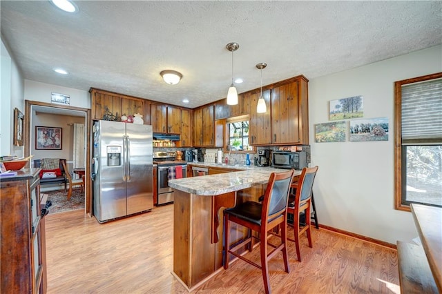 kitchen with pendant lighting, light wood-type flooring, a textured ceiling, appliances with stainless steel finishes, and kitchen peninsula