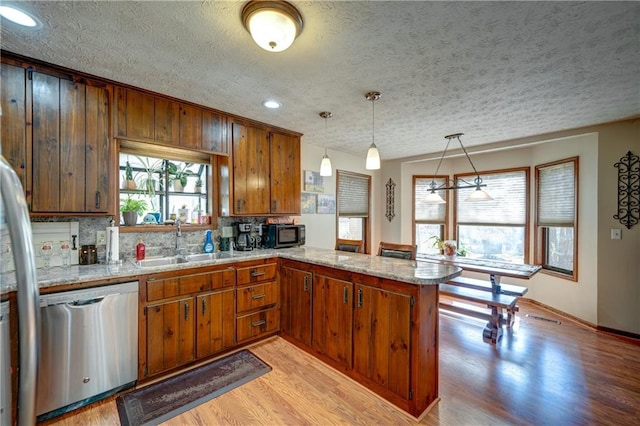 kitchen with sink, light hardwood / wood-style flooring, a textured ceiling, appliances with stainless steel finishes, and kitchen peninsula