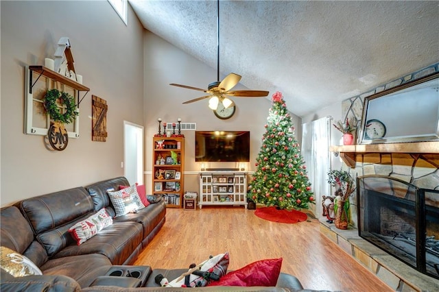 living room featuring a wealth of natural light, a textured ceiling, ceiling fan, hardwood / wood-style flooring, and a stone fireplace