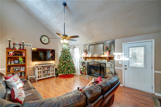 living room with lofted ceiling, hardwood / wood-style flooring, ceiling fan, a fireplace, and a textured ceiling