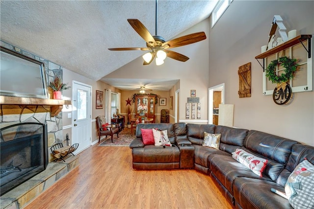 living room featuring a stone fireplace, lofted ceiling, a textured ceiling, and light wood-type flooring