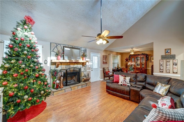 living room with ceiling fan, high vaulted ceiling, hardwood / wood-style floors, a textured ceiling, and a fireplace