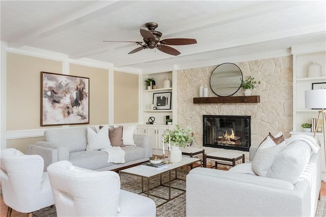 living area featuring built in features, beamed ceiling, a fireplace, and ceiling fan