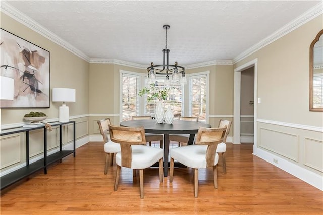 dining room with crown molding, a chandelier, light wood-style flooring, wainscoting, and a textured ceiling