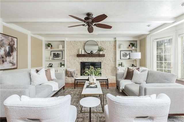 living room with beam ceiling, a ceiling fan, built in features, wood finished floors, and a stone fireplace