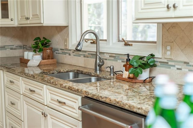 kitchen with tasteful backsplash, dishwasher, light stone countertops, and a sink