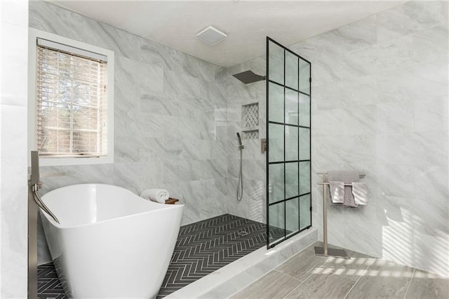 full bath with tile walls, a walk in shower, and a freestanding bath