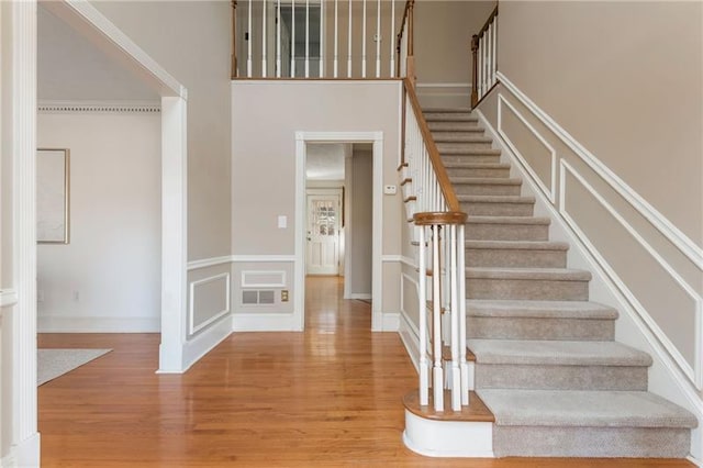 staircase with wood finished floors, a towering ceiling, and a decorative wall