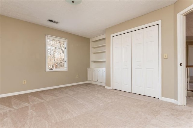 unfurnished bedroom with visible vents, light colored carpet, a textured ceiling, and baseboards