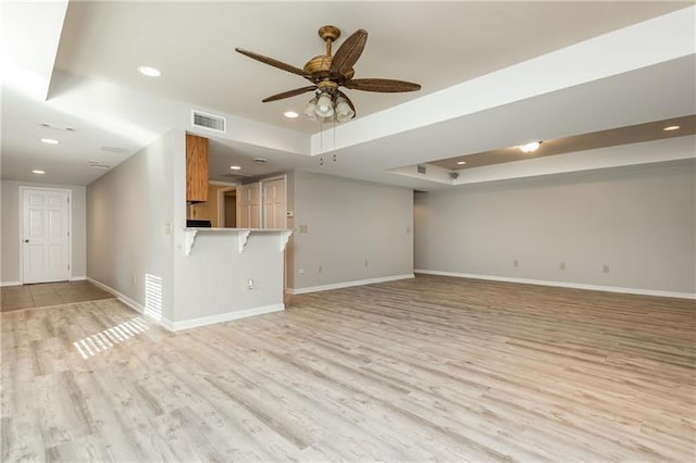 unfurnished living room featuring visible vents, baseboards, light wood-type flooring, and a tray ceiling