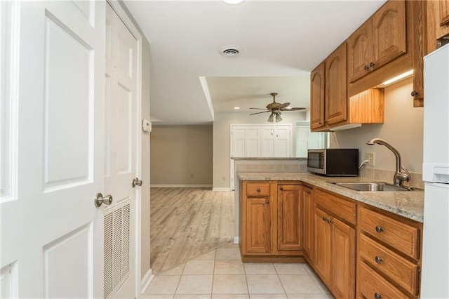 kitchen with stainless steel microwave, visible vents, light stone countertops, light tile patterned flooring, and a sink