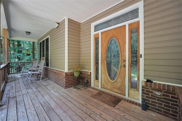 doorway to property featuring a porch and brick siding