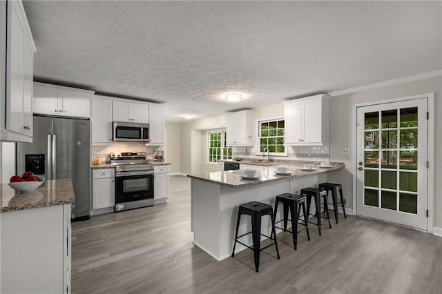 2694 Hickory Valley Dr, Snellville, GA 30078 - kitchen with stainless steel appliances, light wood-style flooring, a peninsula, decorative backsplash, and white cabinetry