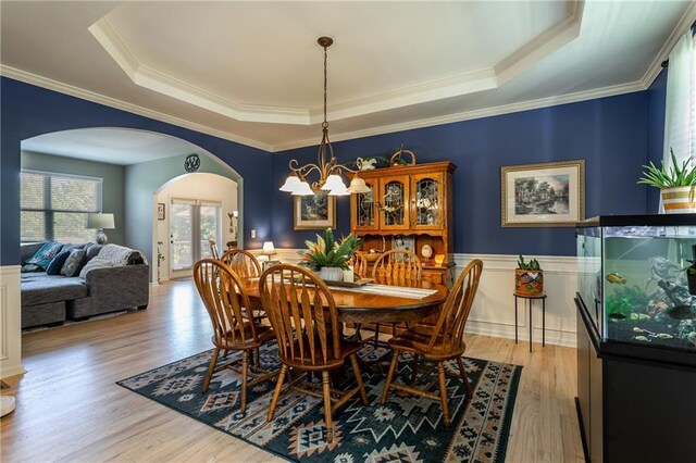 dining space featuring crown molding, a notable chandelier, a tray ceiling, and light hardwood / wood-style flooring