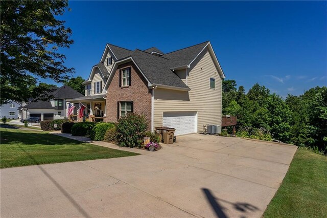 view of side of property featuring central AC unit, a garage, a lawn, and covered porch