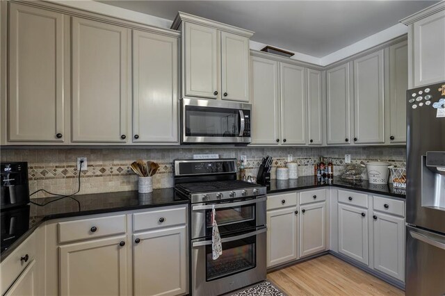 kitchen featuring stainless steel appliances, decorative backsplash, light hardwood / wood-style floors, and dark stone counters