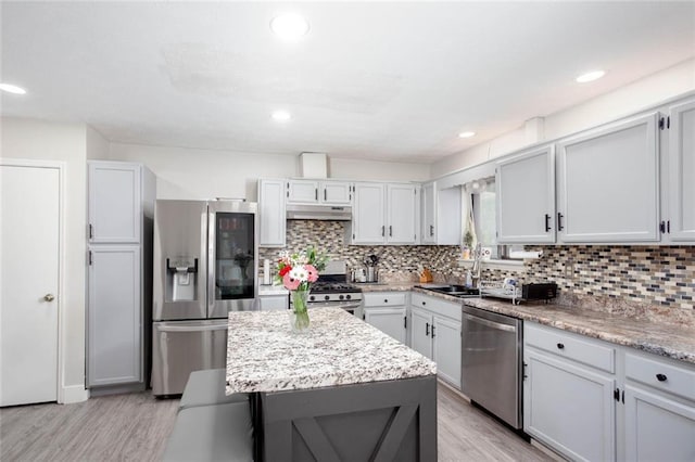 kitchen with stainless steel appliances, under cabinet range hood, tasteful backsplash, a sink, and recessed lighting