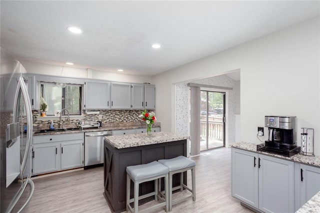 kitchen featuring stainless steel appliances, a sink, light wood finished floors, backsplash, and a kitchen breakfast bar