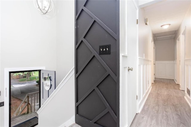 hallway with light wood-style flooring, a decorative wall, and a wainscoted wall