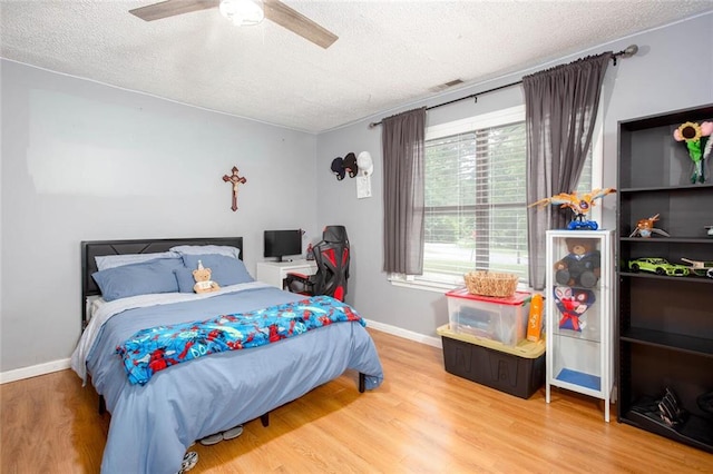 bedroom with a textured ceiling, wood finished floors, baseboards, and ceiling fan