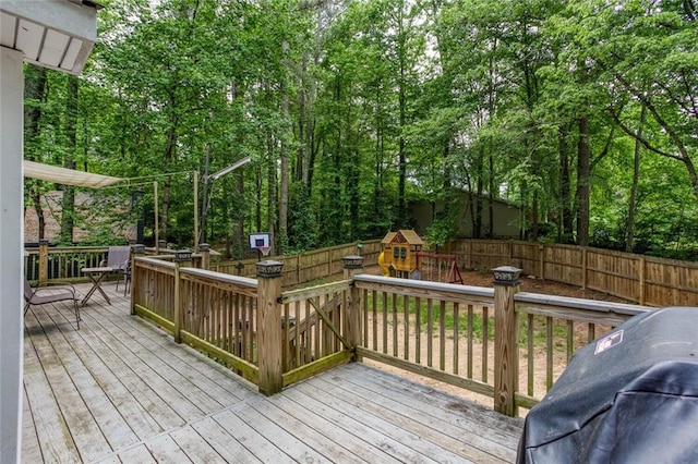 wooden terrace with a playground, fence, and grilling area