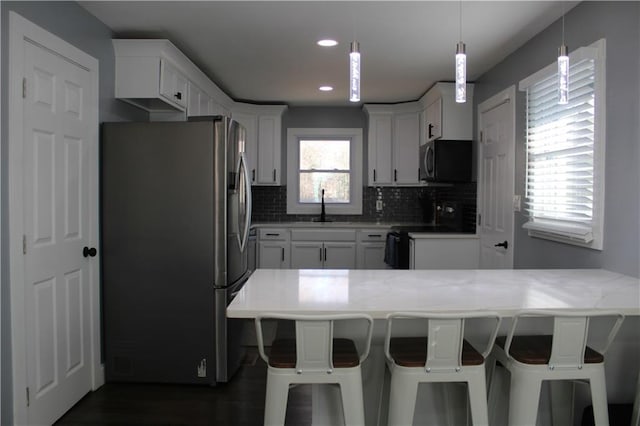 kitchen with stainless steel refrigerator with ice dispenser, range with electric cooktop, a kitchen breakfast bar, and pendant lighting