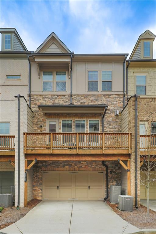 rear view of house with a garage, stone siding, central AC unit, and concrete driveway