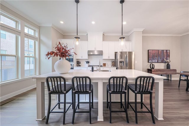 kitchen with tasteful backsplash, stainless steel fridge with ice dispenser, a large island with sink, under cabinet range hood, and a sink