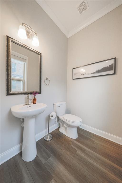 half bathroom featuring visible vents, toilet, ornamental molding, wood finished floors, and baseboards